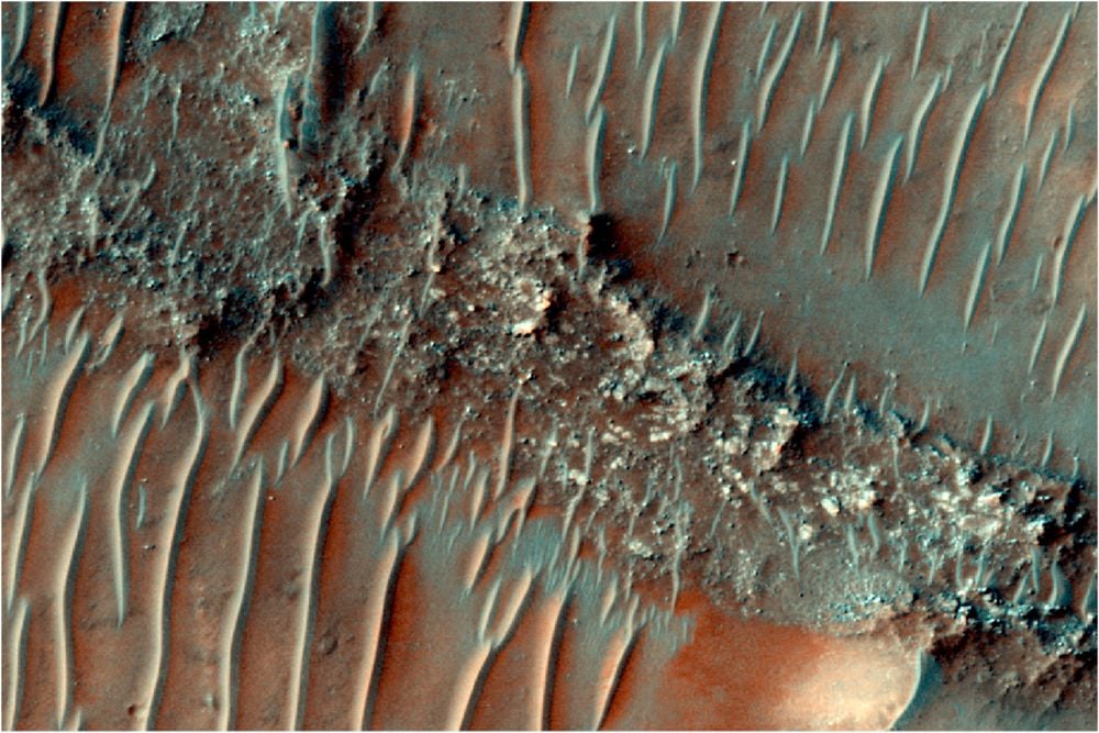 This color image from the MRO's HiRISE camera shows a flat topped, heavily eroded fluvial sinuous ridge (FSR) on Mars. Sand dunes can be seen migrating over the top of the FSR. FSRs are created when rivers deposit sediment. The sediments hardens until it's harder than the surrounding terrain. As aeolian erosion wears down the softer, surrounding rock, the FSR is left behind as evidence of the ancient river. HiRISE Image: ESP_085386_1505. Image Credit: NASA/JPL/University of Arizona. Licence type: Attribution (CC BY 4.0)