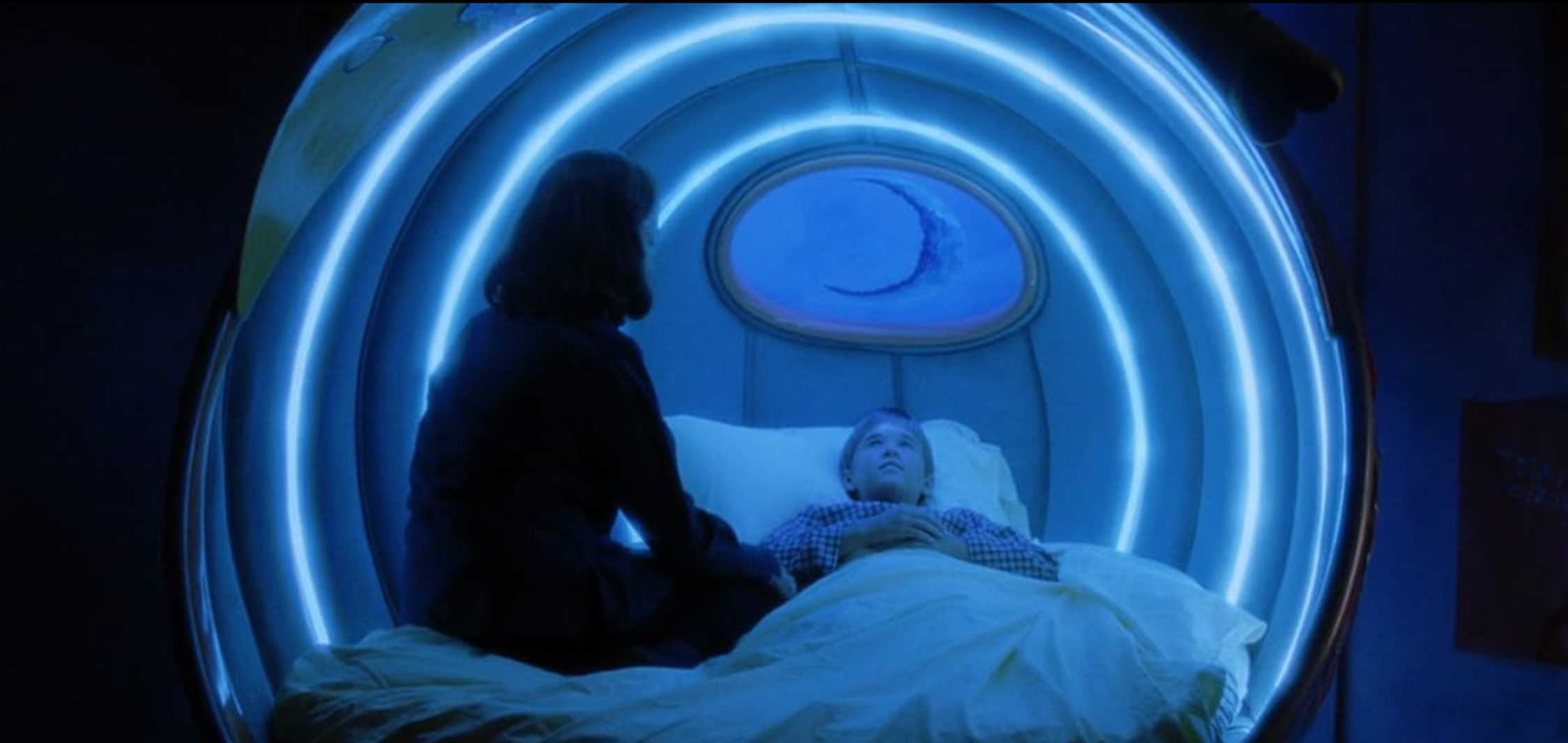 a woman in a blue-lit sleeping chamber with a child in bed