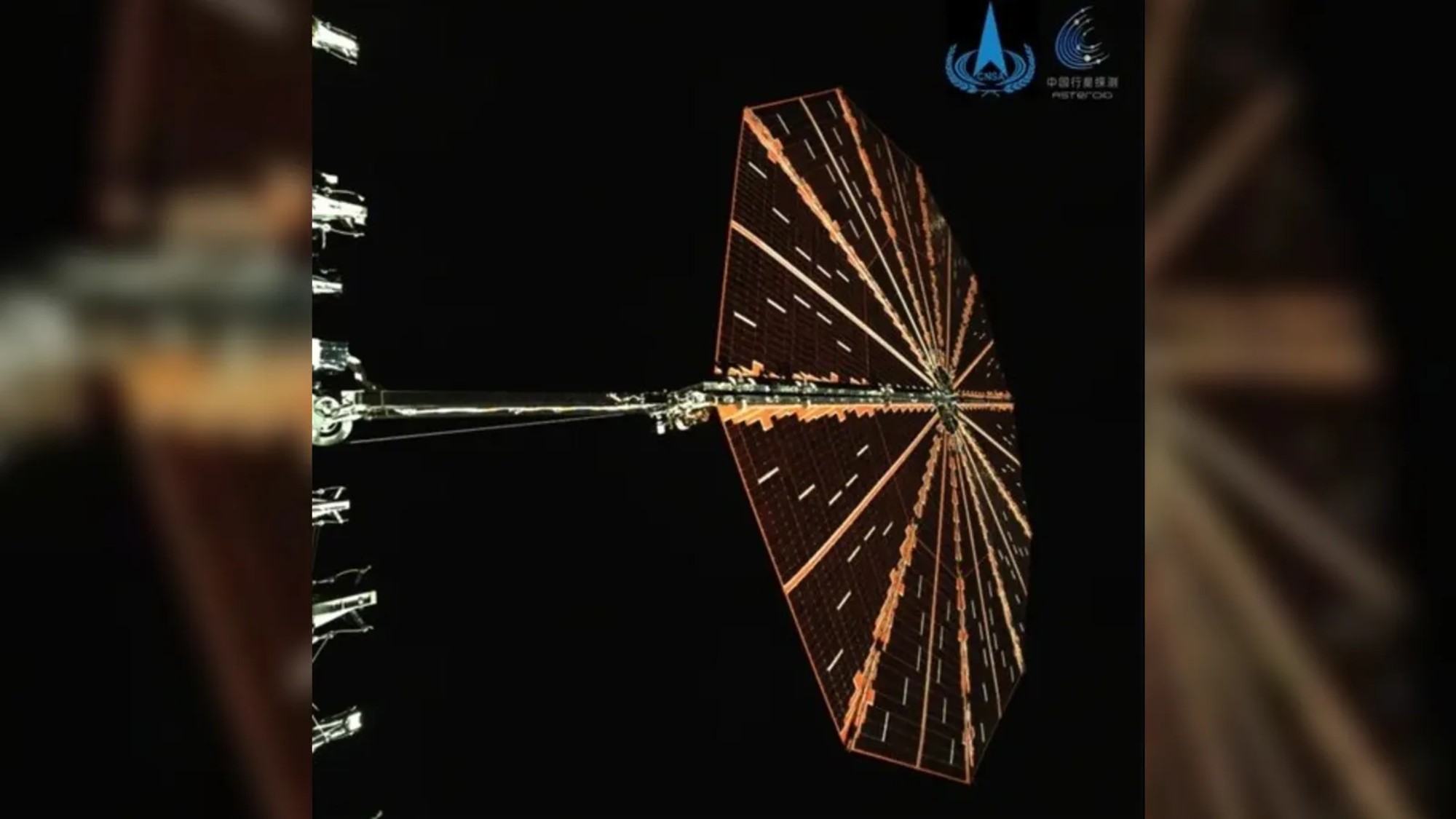 an octagonal solar panel on the end of a metal arm that extends outward from a metallic rectangle, just out of view on the left side of the image