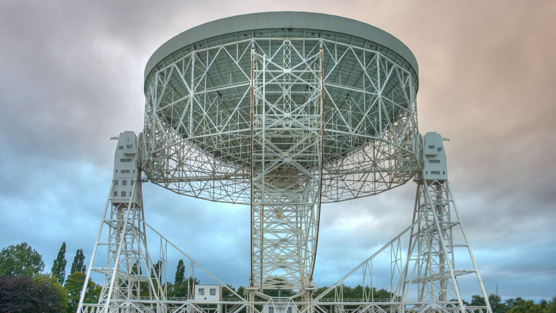 A photo of a white large structure with lots of poles holding it up. The poles conglomerate into some large stands that look like