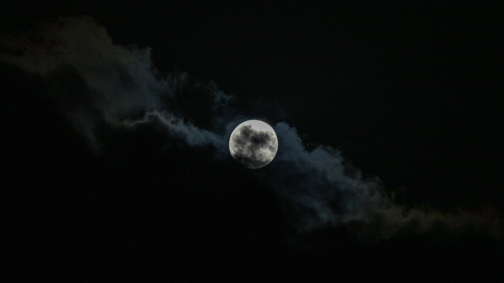 A silver full moon glows in a dark sky behind a bank of encroaching cloud.
