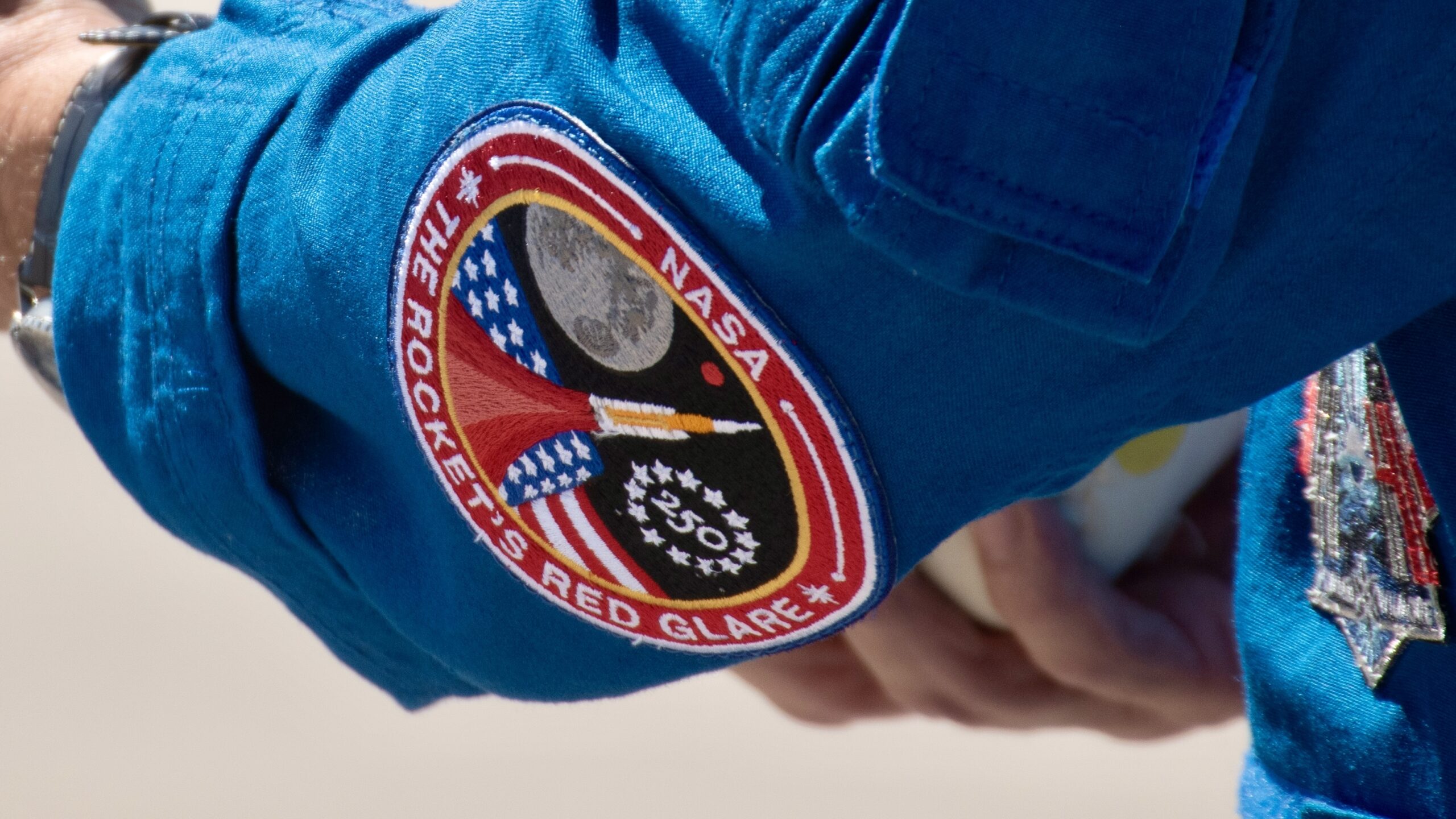 the back of someone's arm wearing a blue sleeve with red-outlined patch near the elbow.