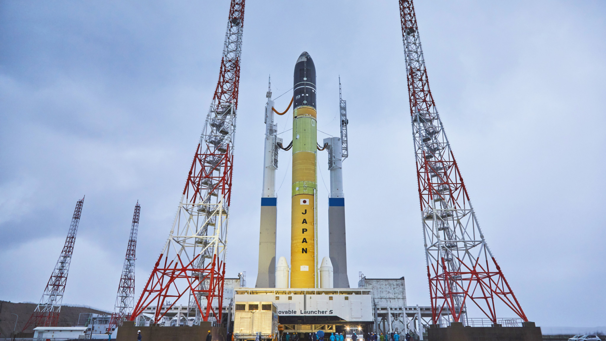 side view of a yellow rocket on a launch pad beneath gray skies