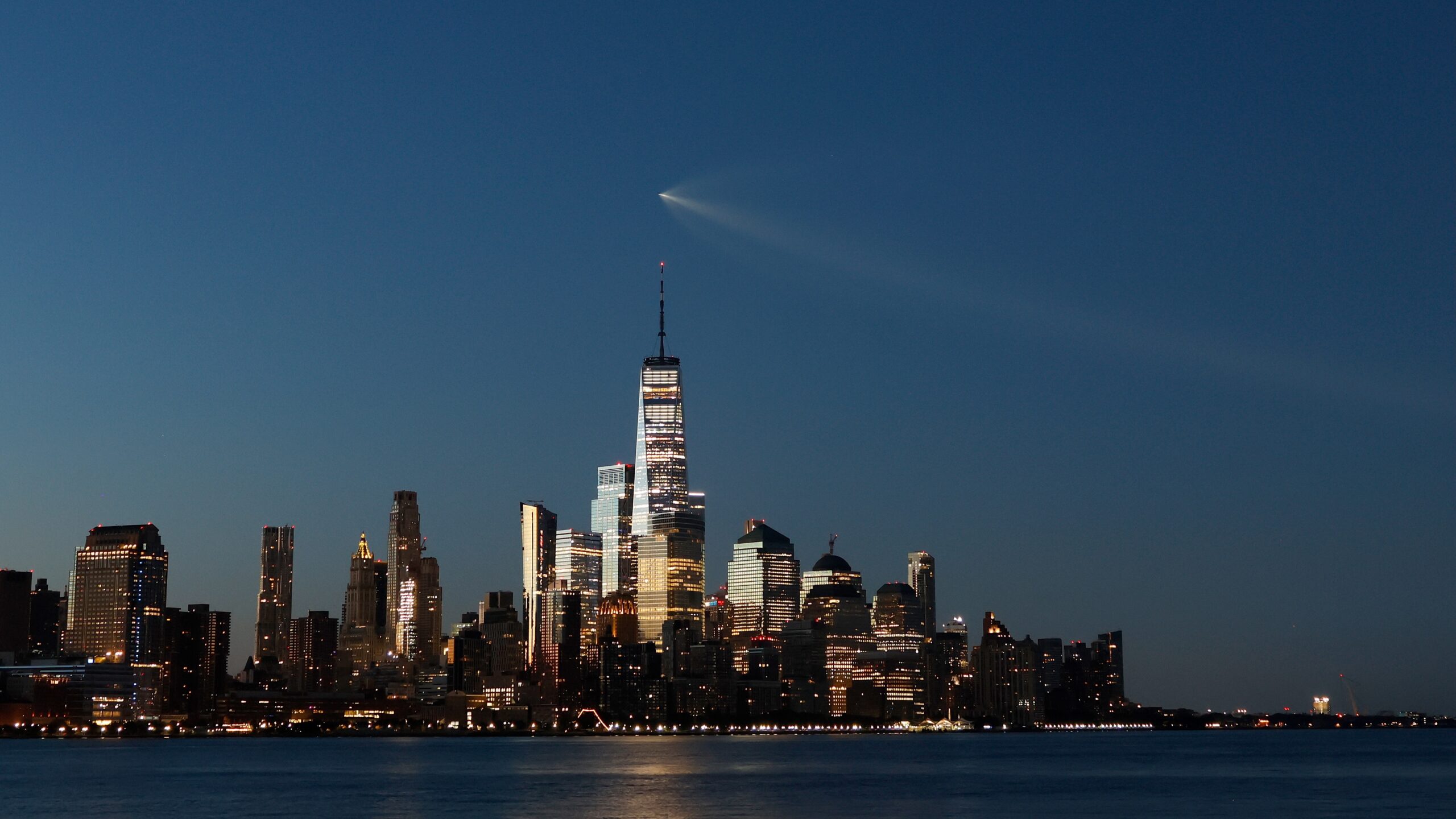long-distance photo of a rocket cruising over the New York City skyline shortly before dawn. the rocket looks kind of like a comet