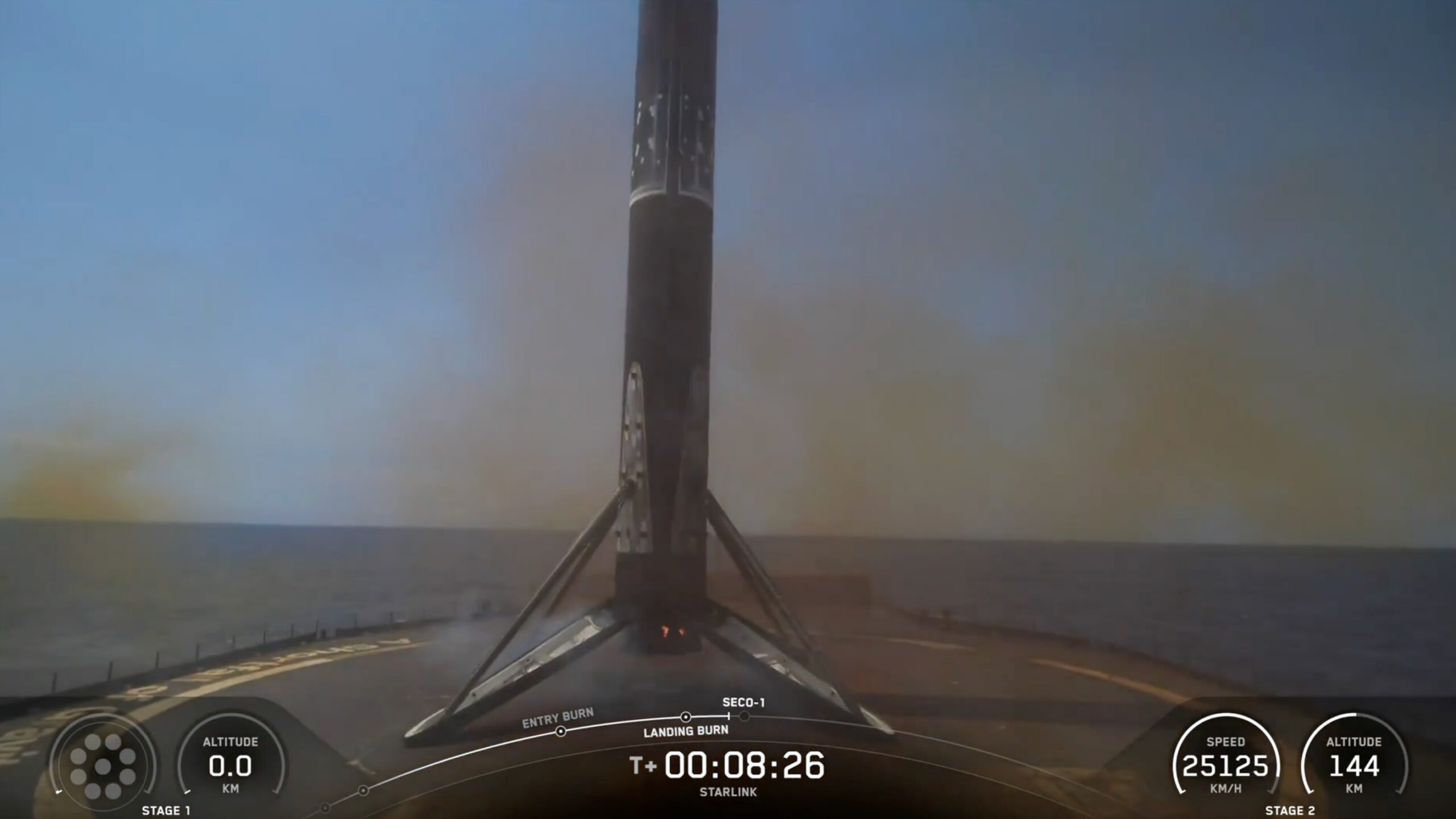 A black and white spacex falcon 9 rocket first stage sits on the deck of a ship at sea.
