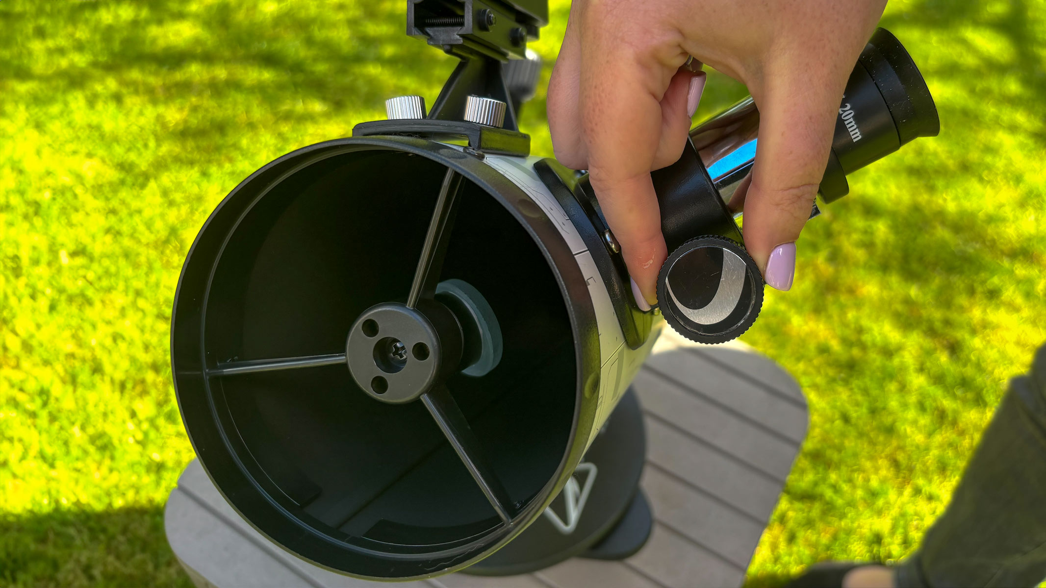 Fingers adjusting the eyepiece on the Celestron Moon Mission 100mm Tabletop Dobsonian with grass in the background.