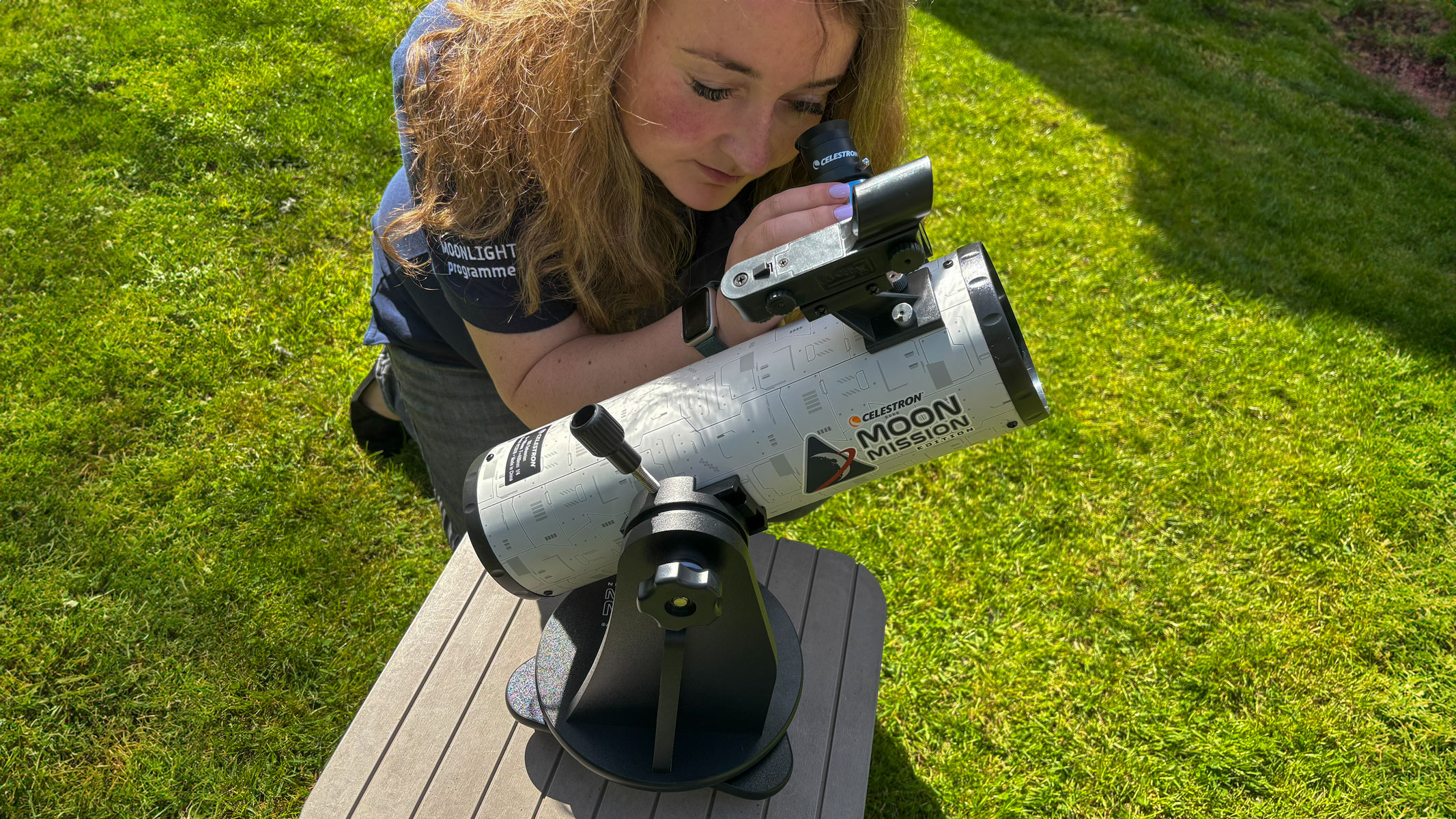 A woman looking through the Celestron Moon Mission 100mm Tabletop Dobsonian with grass in the background.