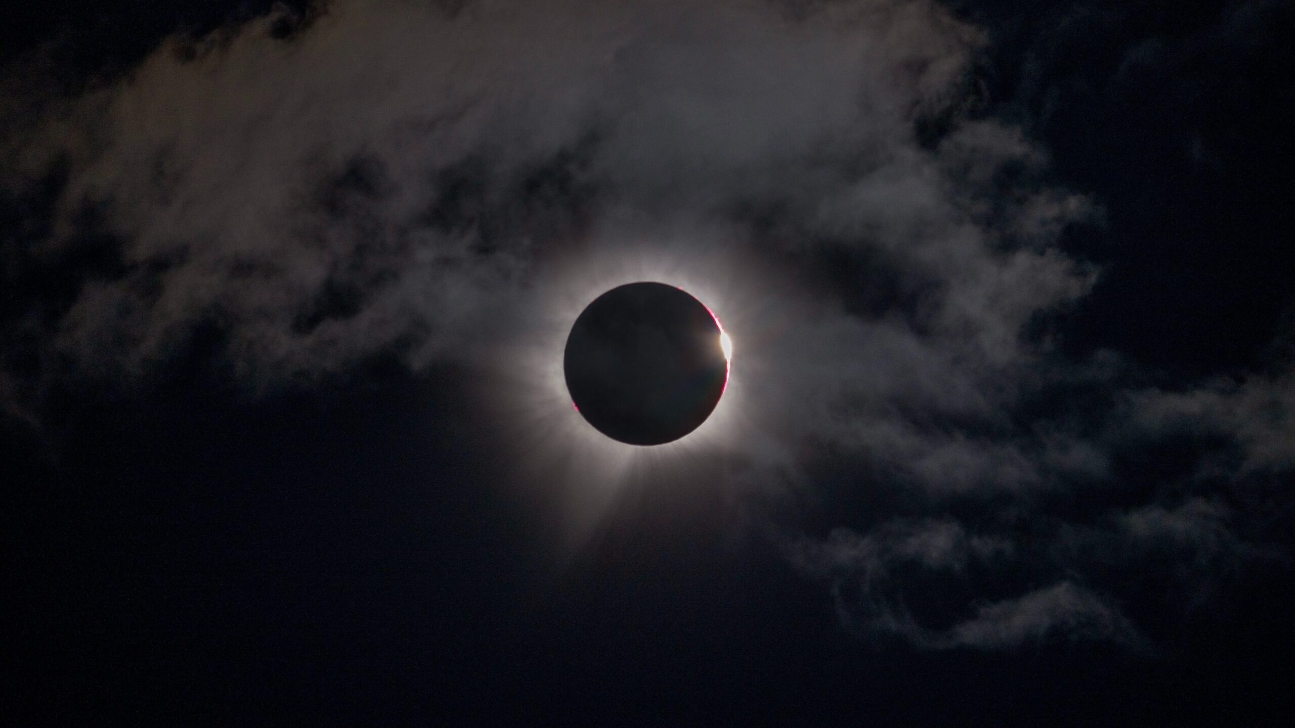 the moon perfectly obscures the sun, leaving a ring of white fiery light in a slightly cloudy sky