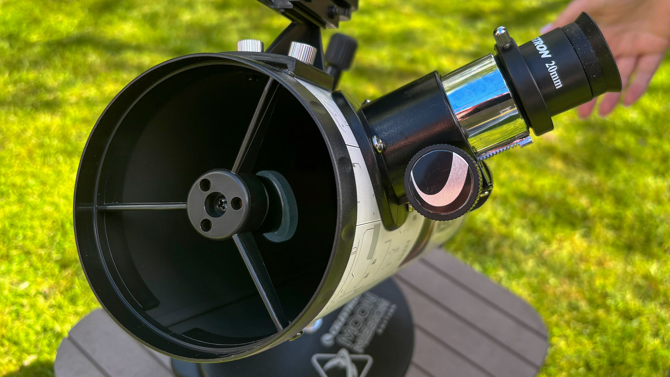 The aperture and eyepiece on the Celestron Moon Mission 100mm Tabletop Dobsonian with grass in the background.