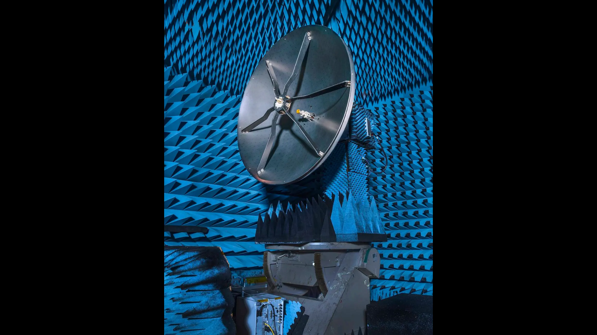 A large dark colored satellite dish style structure in a blue insulated room.
