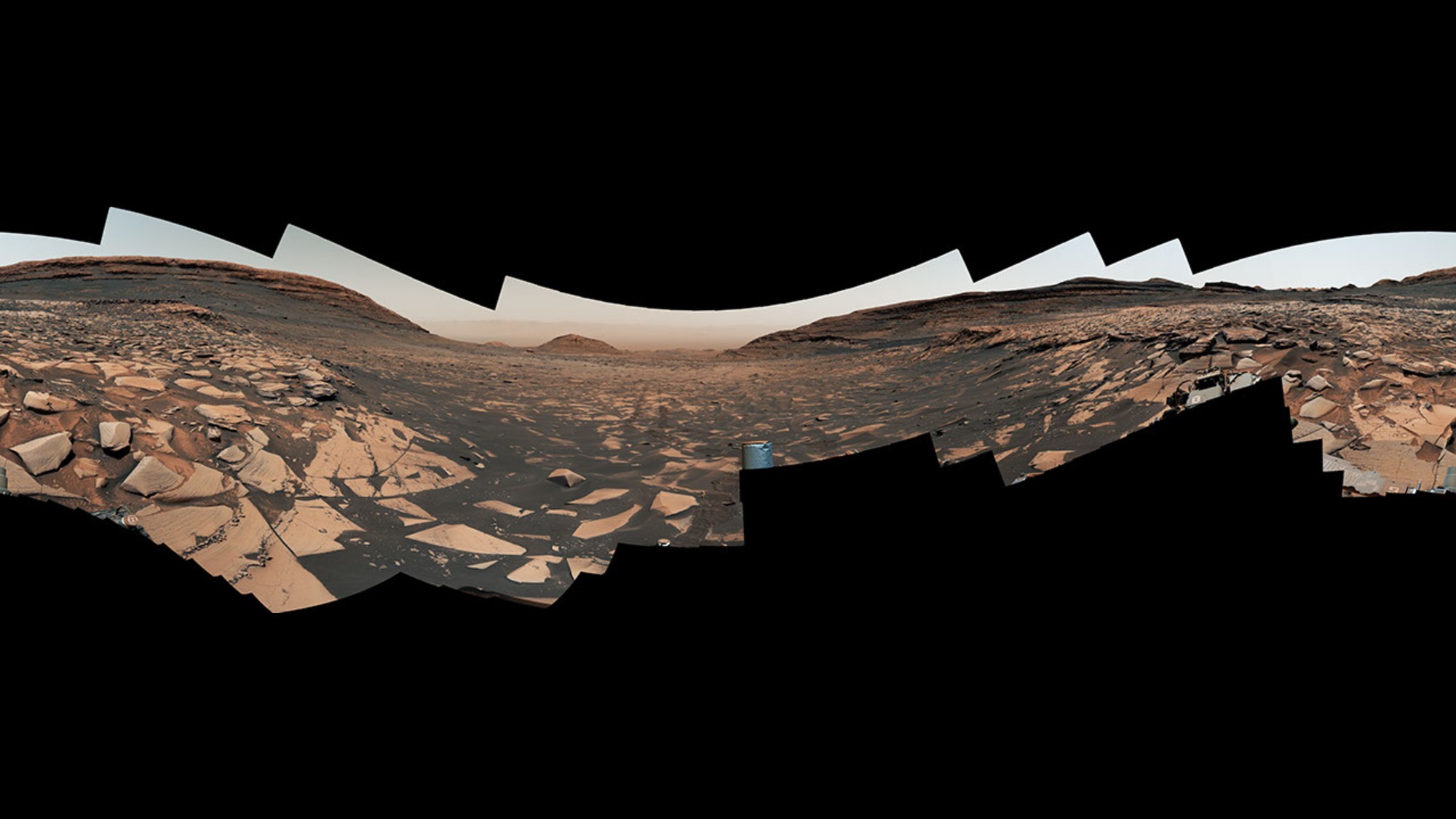 a panoramic image showing a reddish orange, dusty landscape