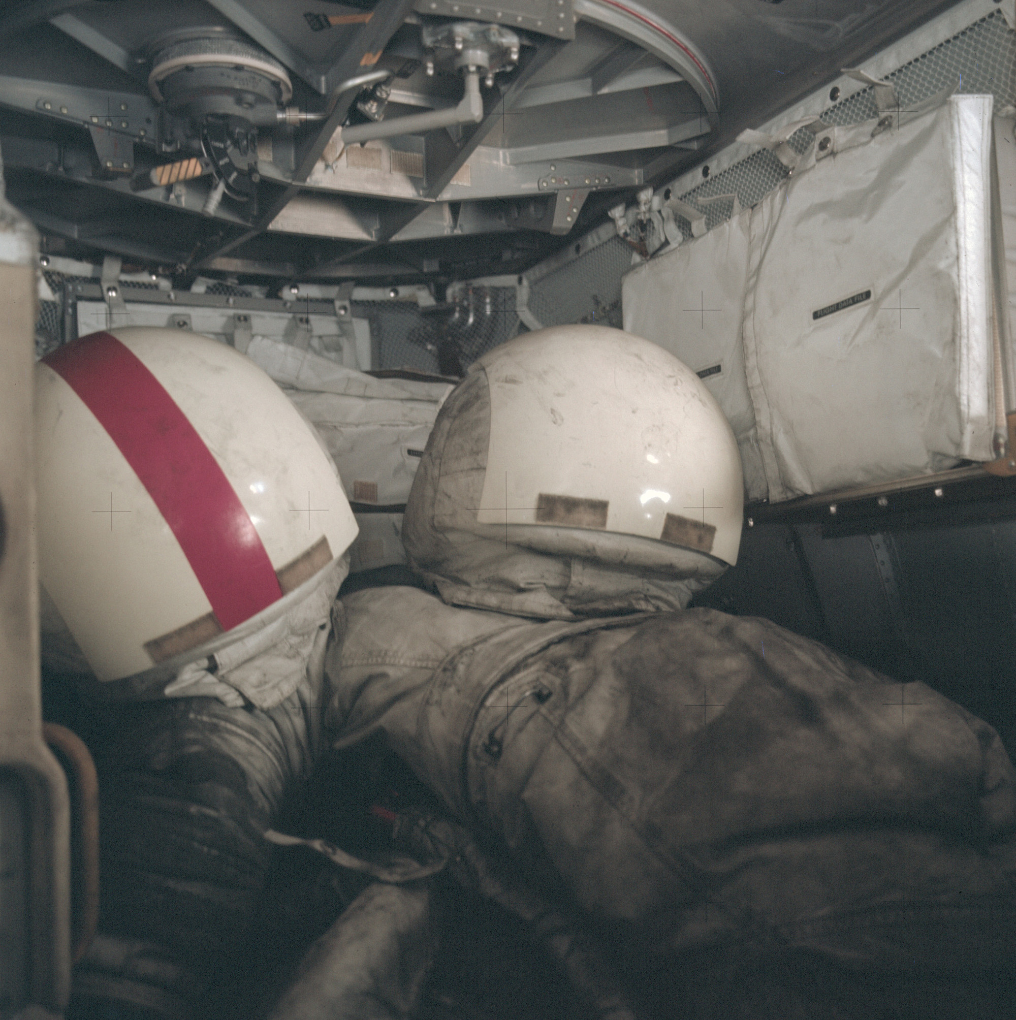 helmets and white spacesuits covered in grey dust inside a cramped metallic cabin