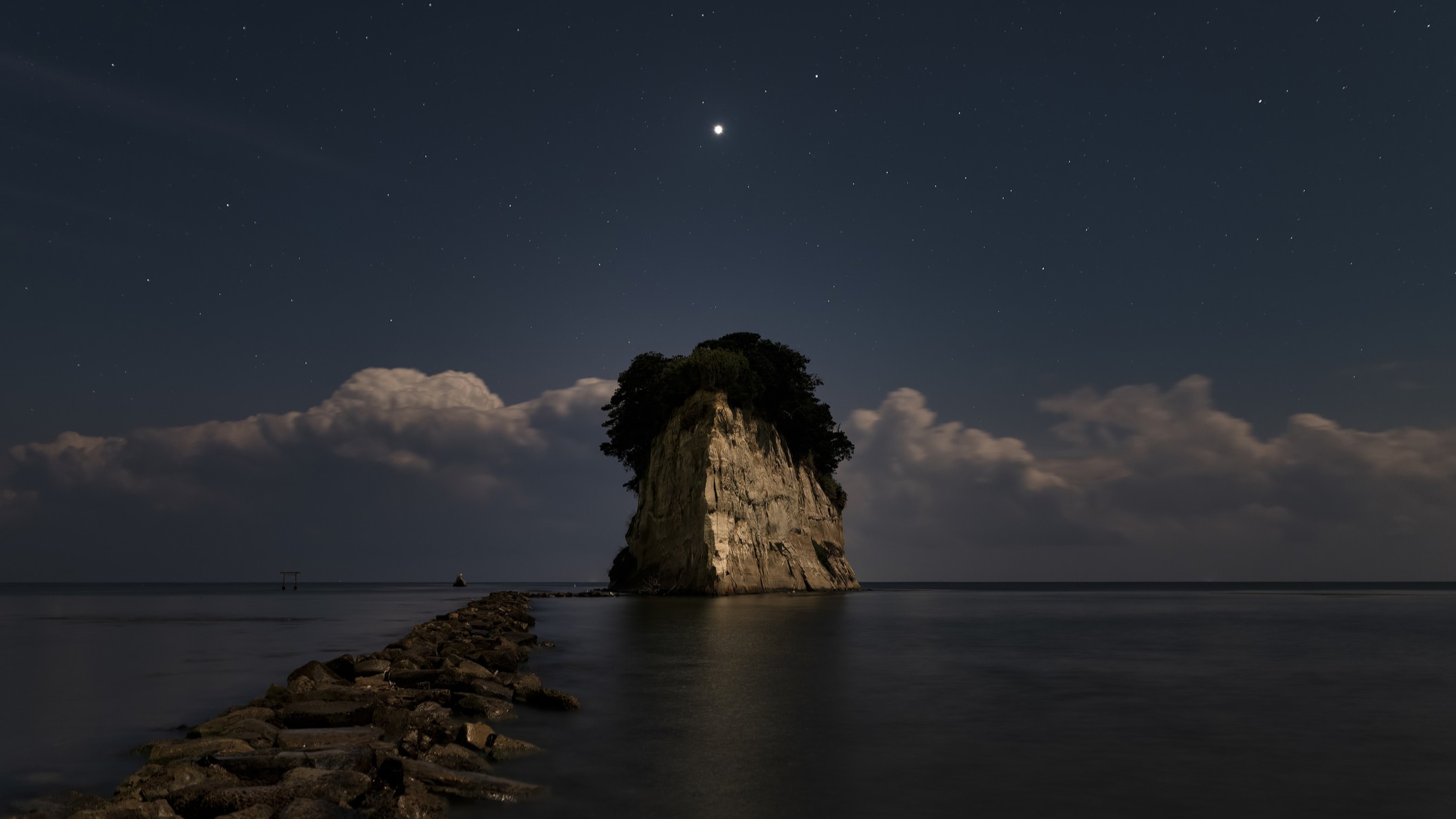a single large rock structure in a body of water with a bright object shining in the sky above.