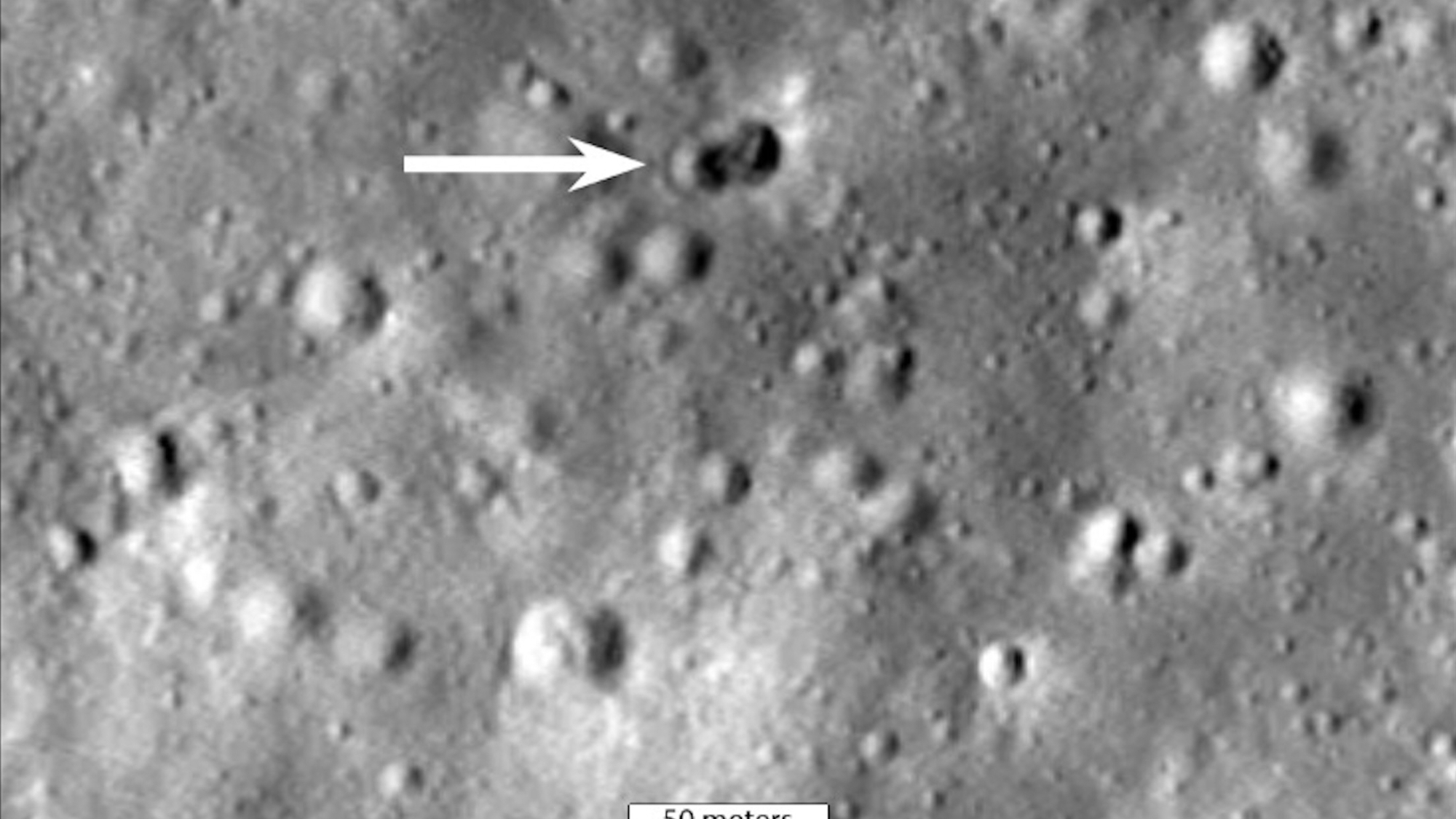 closeup of the cratered lunar surface, with a white area pointing to a newly formed double crater