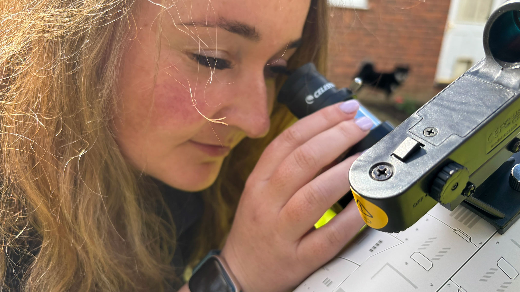A woman looking through the eyepiece of the Celestron Moon Mission 100mm Tabletop Dobsonian.