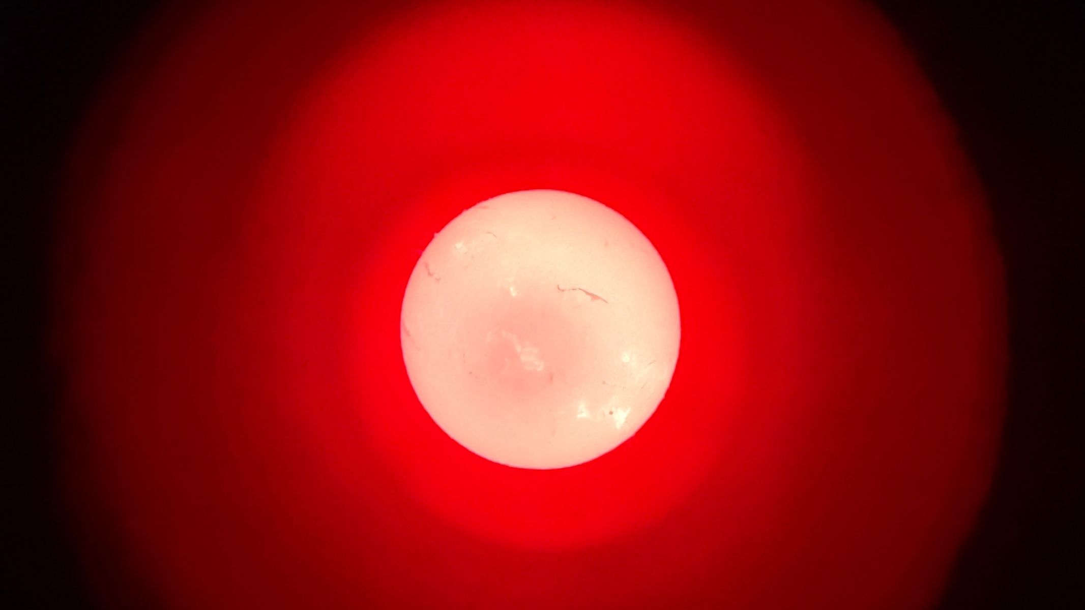 The red solar disk, showing detail on the surface and surrounded by red and black, as imaged with a smartphone.