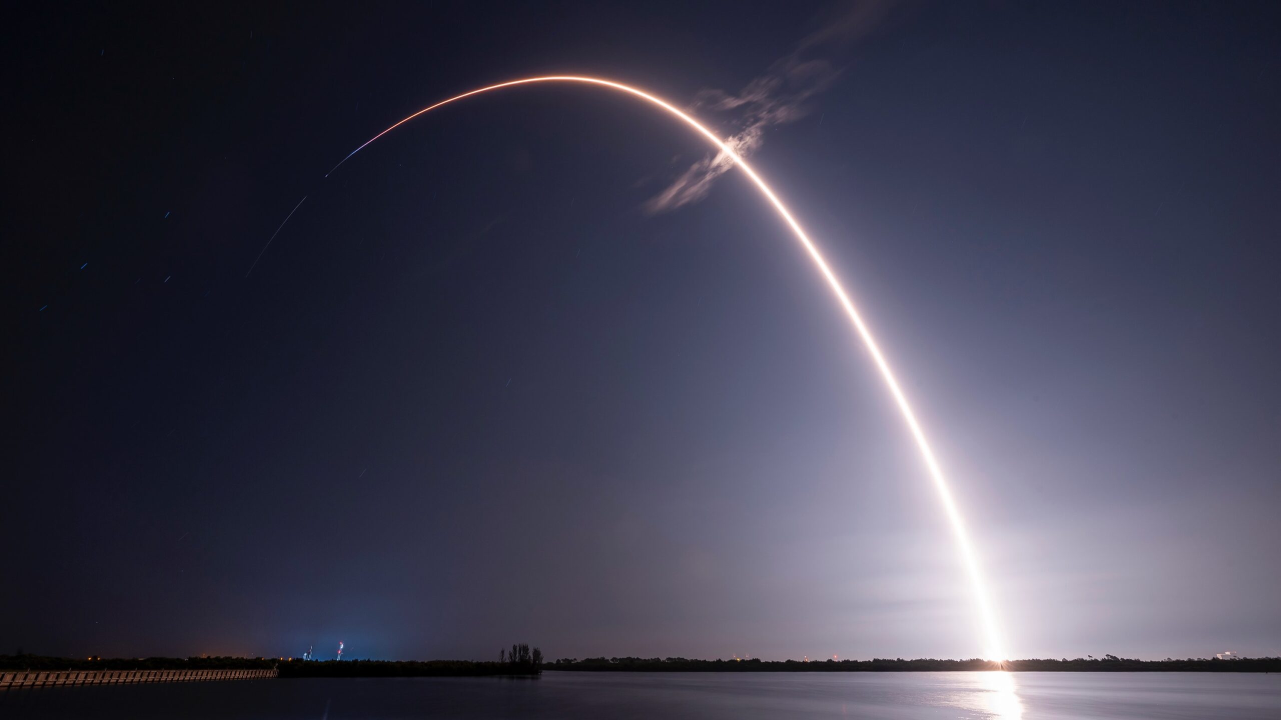 A rocket launch carves an orange arc into a dark night sky in this long-exposure photo.