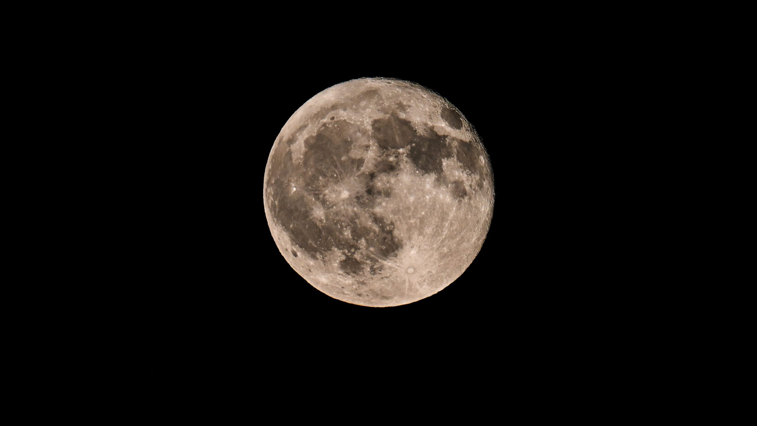 A full moon is photographed in a black night sky with dark lunar seas and craters marking its surface.
