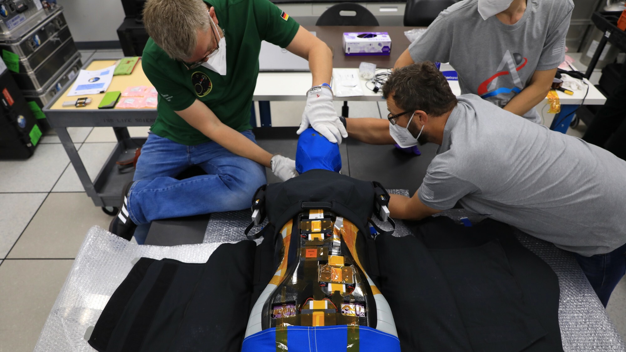 two men assemble a bluish torso-only mannequin on a table