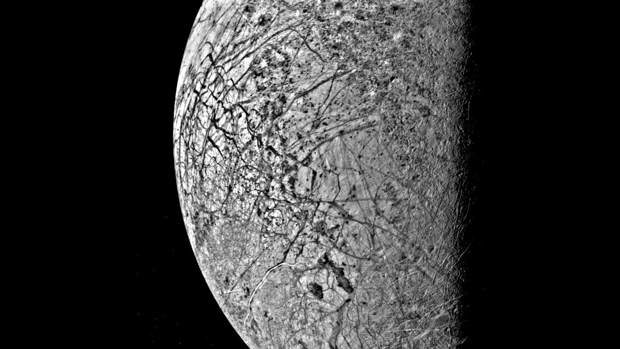 darkness obscures half of a grey orb crisscrossed with deep lines and cracks
