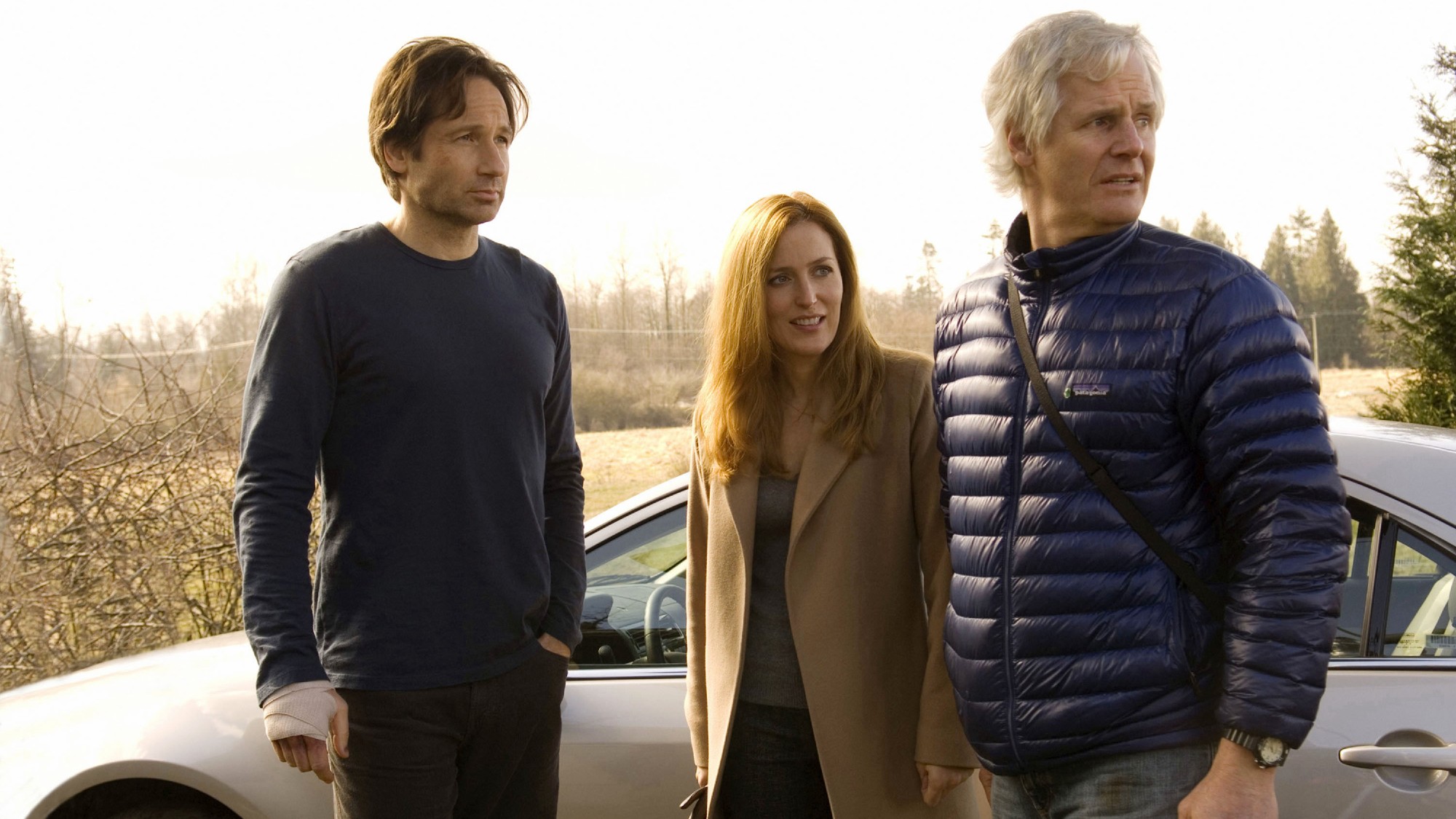 three people in winter clothing in front of a parked car in a field