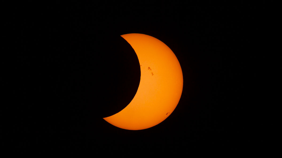 A partial solar eclipse with an orange sun with sun spots.