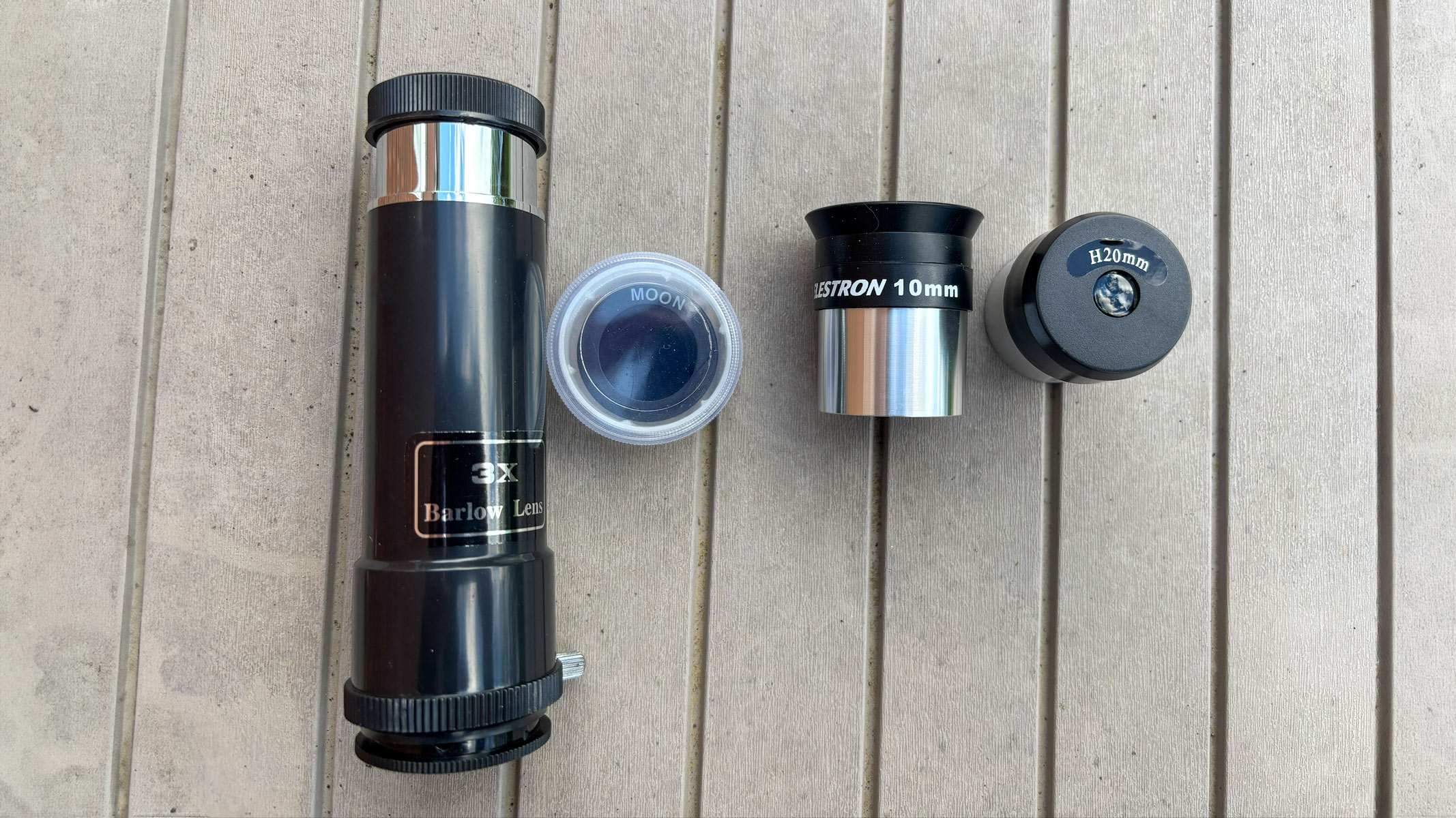 Different eyepieces for the Celestron Moon Mission 100mm Tabletop Dobsonian on a grey table.
