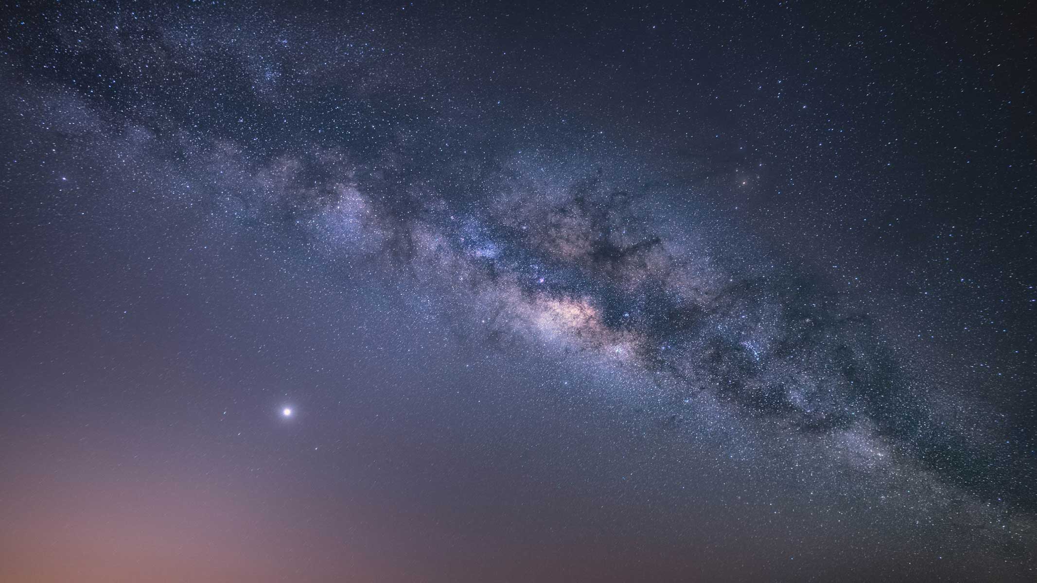 Milky way galaxy in the night sky stretching across the image in a thick band of stars.