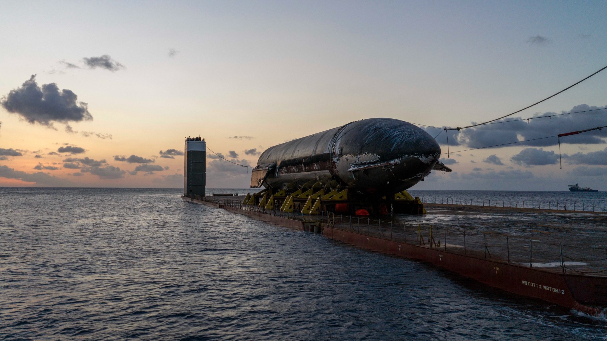 a cylindrical black spacecraft on the deck of a ship at sea at dusk