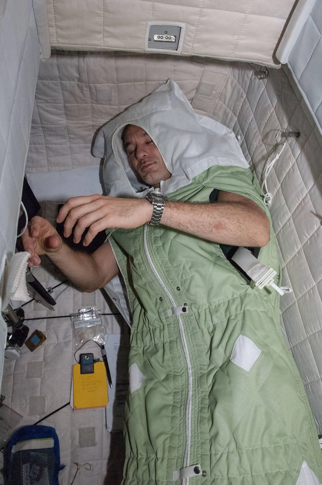 A crew member secured in a sleep restraint inside their personal crew quarters aboard the International Space Station, one of the small, private spaces designers have learned matter enormously to a crew's sense of home (Credit : NASA)