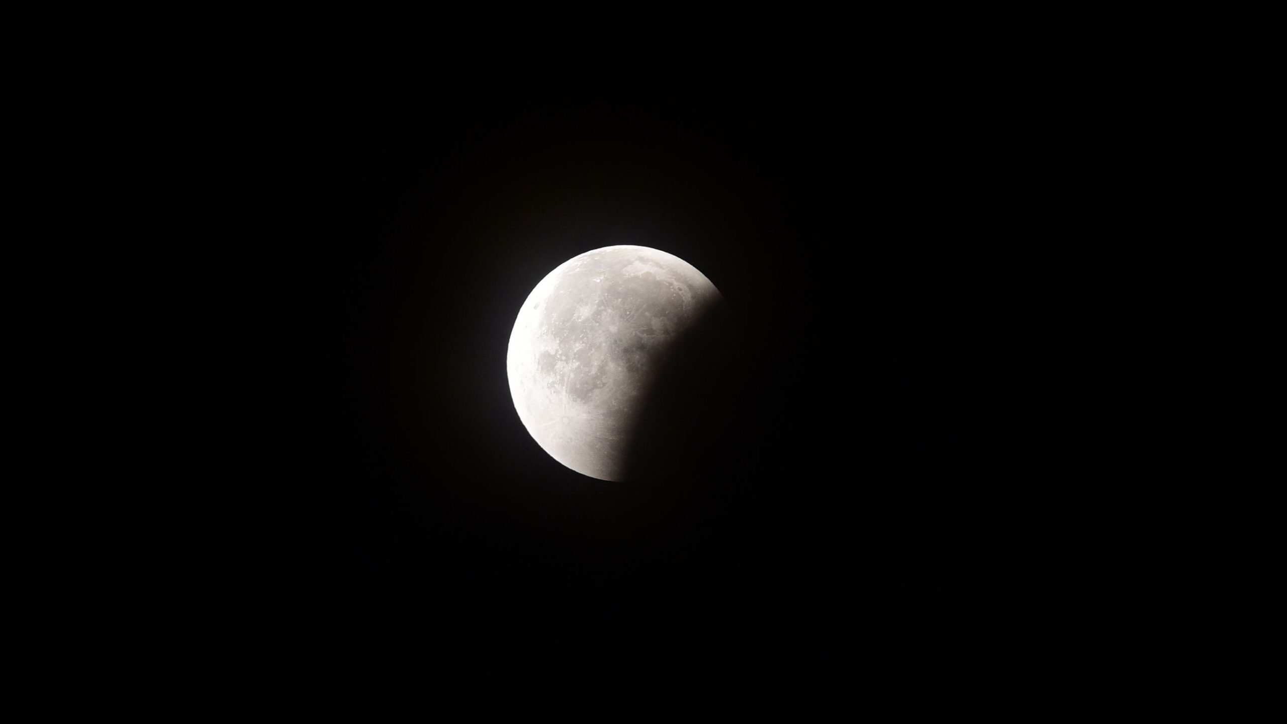 A full moon is photographed in a black sky with its lower right portion hidden by Earth's curved shadow during a lunar eclipse.
