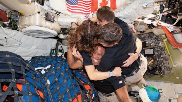 three men and one woman hug inside a space capsule