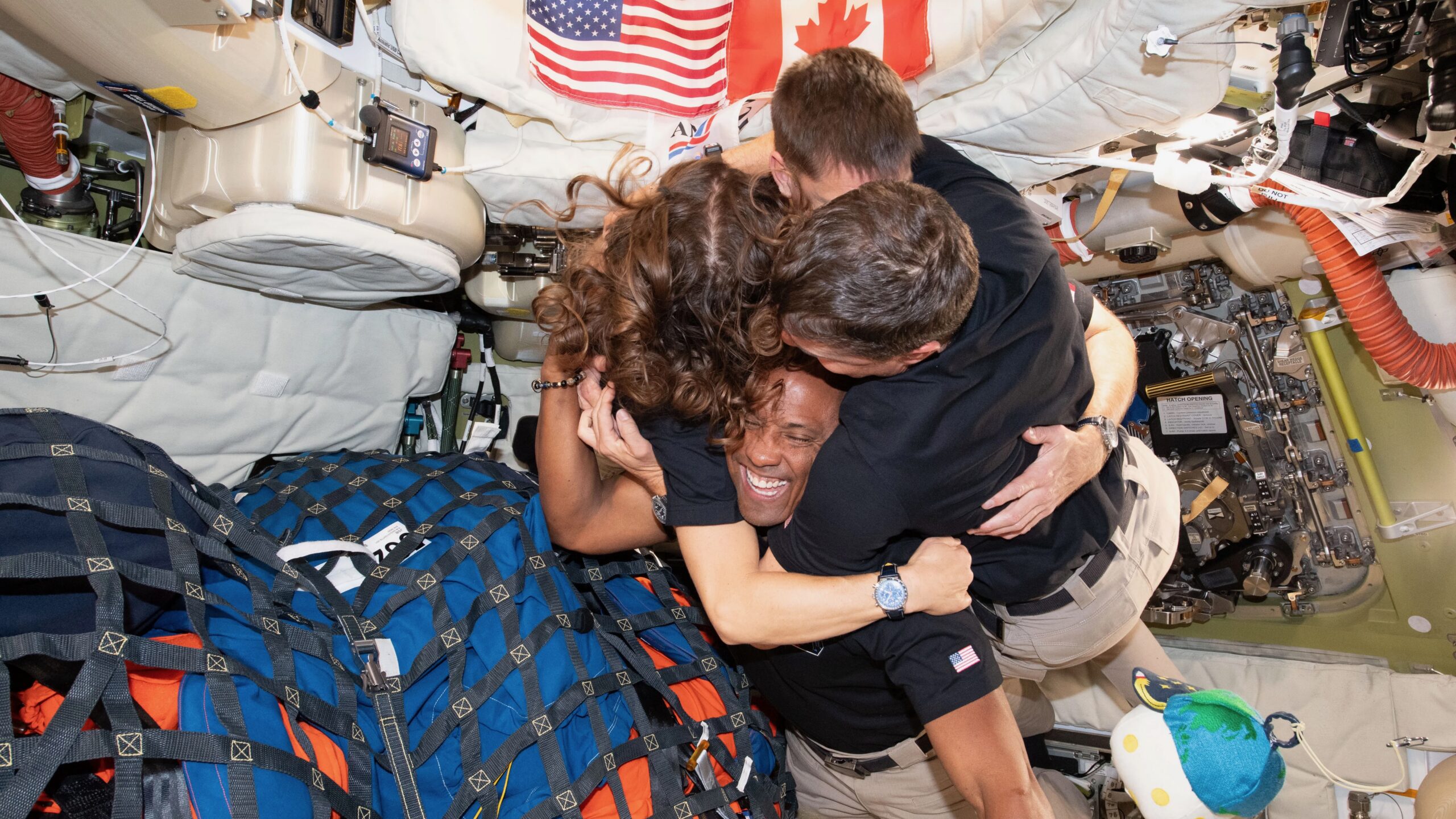 three men and one woman hug inside a space capsule