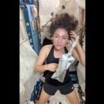 a woman wearing a black tank top and black shorts holds a water bottle on board a space station