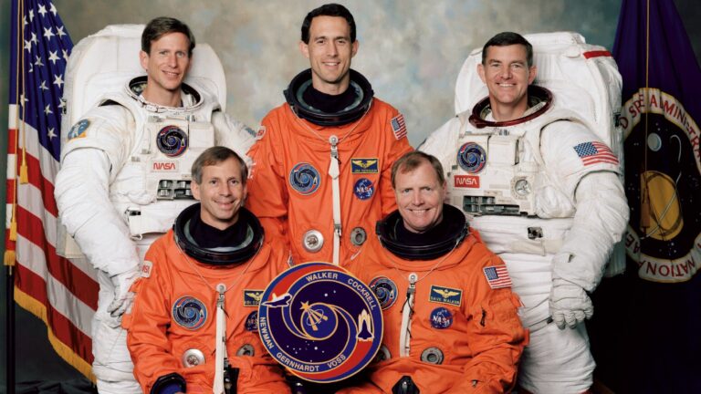 Five astronauts, two in white spacewalking suits and three in orange launch suits, post for an STS-69 NASA shuttle crew portrait.