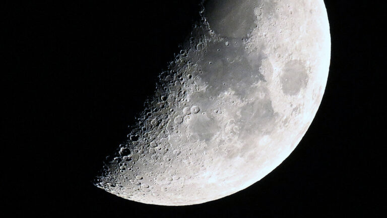 A photo of the moon with its right side lit around the first quarter phase in a black sky.