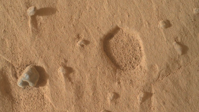 A close-up of the Martian surface with a wide, shallow pit.