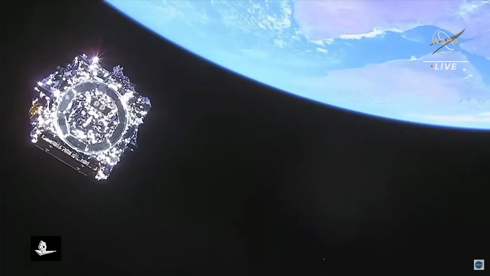 Photograph from a NASA Live broadcast showing a spacecraft against the blackness of space, its reflective solar panels and faceted gold and silver surfaces catching sunlight at left, with the curved blue limb of Earth and white clouds filling the upper right corner. The NASA logo and LIVE label appear at upper right, with a small mission logo at lower left.