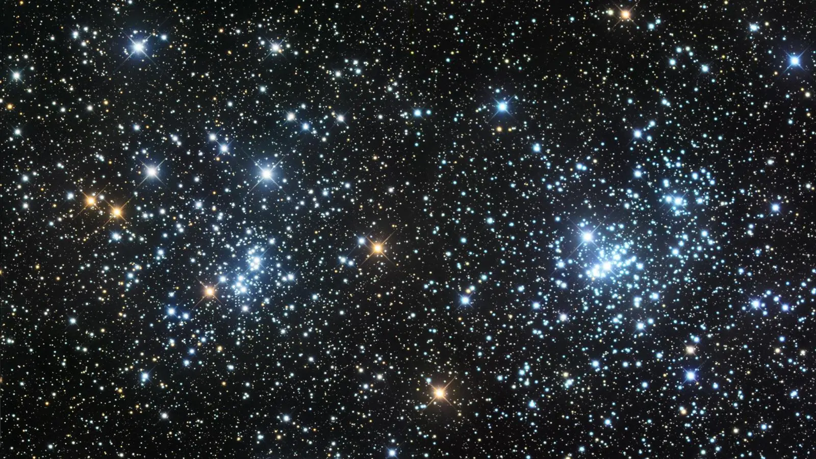 Photograph of the Double Cluster, showing two dense groupings of blue-white and orange stars side by side against a black sky thickly populated with fainter background stars, with the brightest stars in each cluster showing prominent diffraction spikes.