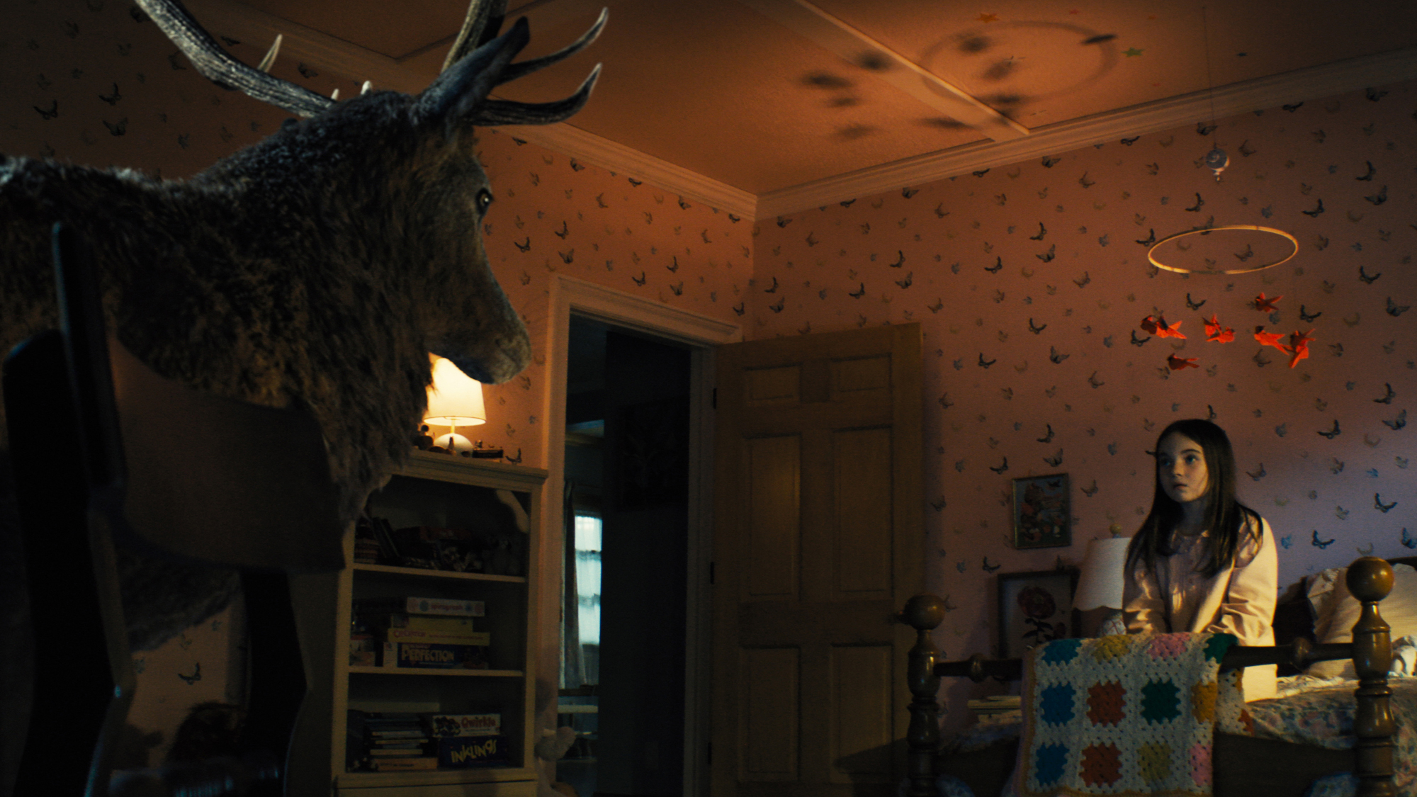 A young girl in her bedroom, staring at a stag at the foot of her bed.