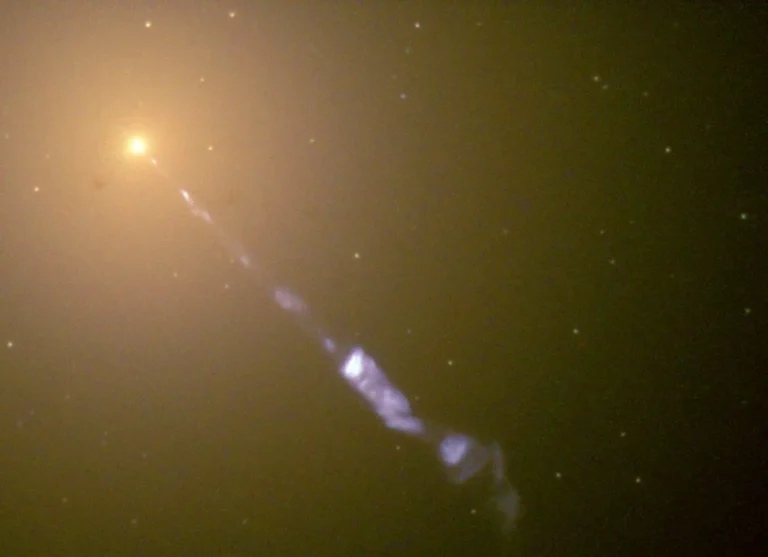 Image taken by the Hubble Space Telescope of a 5000-light-year-long jet ejected from the active galaxy M87. The blue synchrotron radiation contrasts with the yellow starlight from the host galaxy. The dots spread around the image are not individual stars, but globular star clusters. Credit: NASA/The Hubble Heritage Team (STScI/AURA)