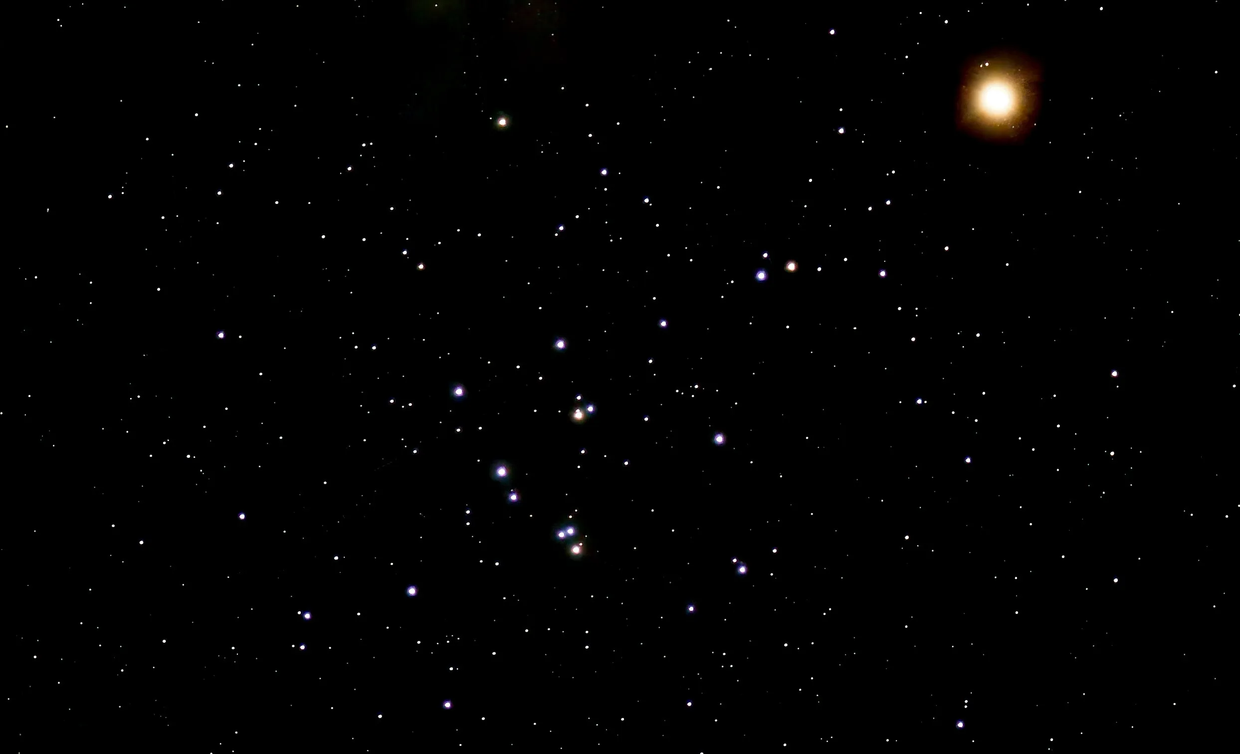 Photograph of the Beehive Cluster (M44) as a loose scattering of blue-white stars with a few orange stars across the lower center of the frame, set against a black sky filled with fainter stars. Mars appears at upper right as a bright, glowing orange-red disk.