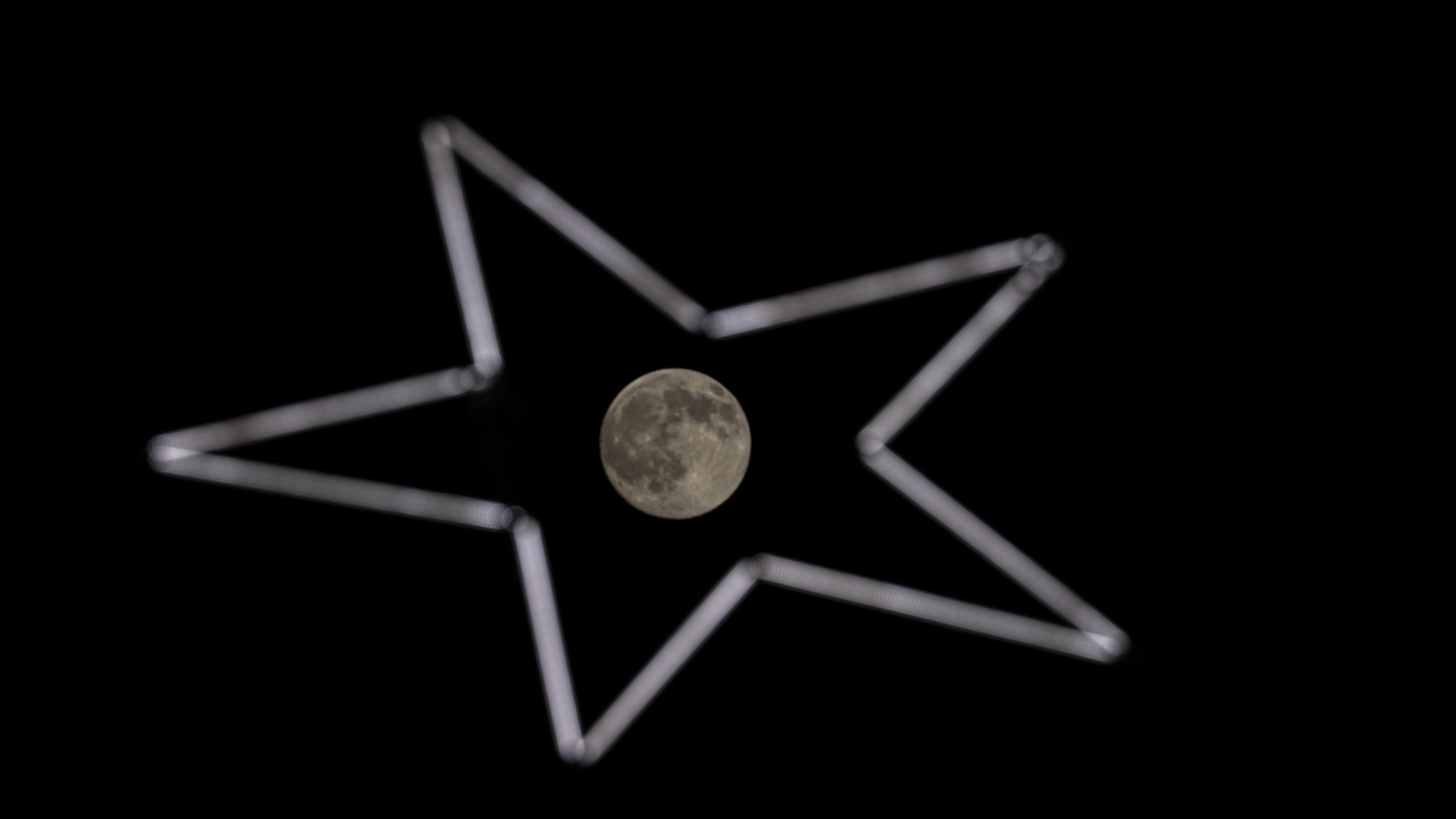 The full moon is photographed in the middle of a star-shaped neon sign at night.