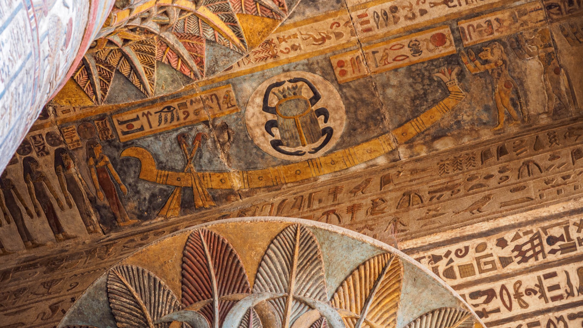 A colorful ceiling depicting ancient Egyptian drawings, such as a scarab, a long boat, people, and hieroglyphics.