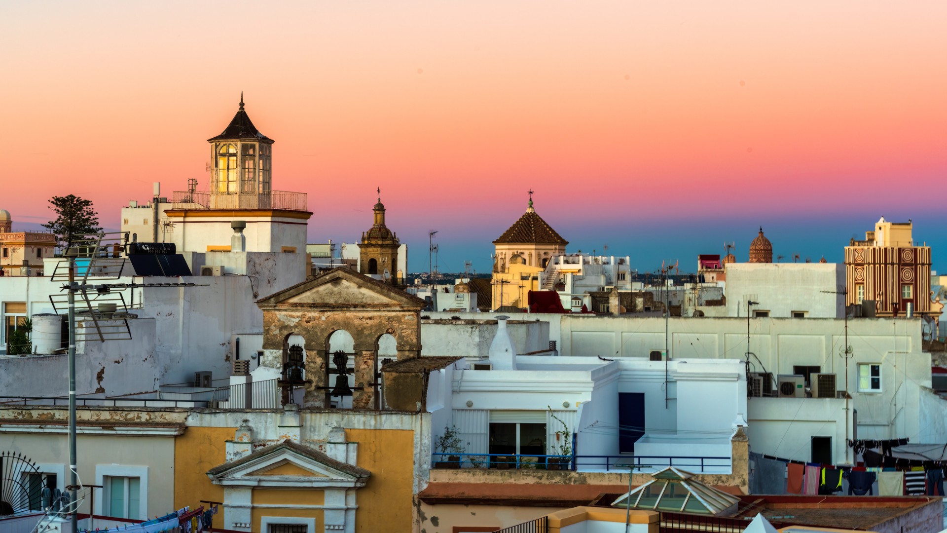 Colorful sunset over a historic city center. There are white and yellow buildings, with several tall towers.